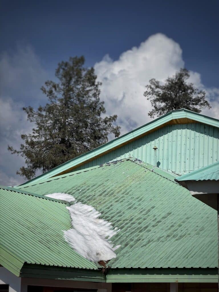 Green metal roofs with snow patches under cloudy sky